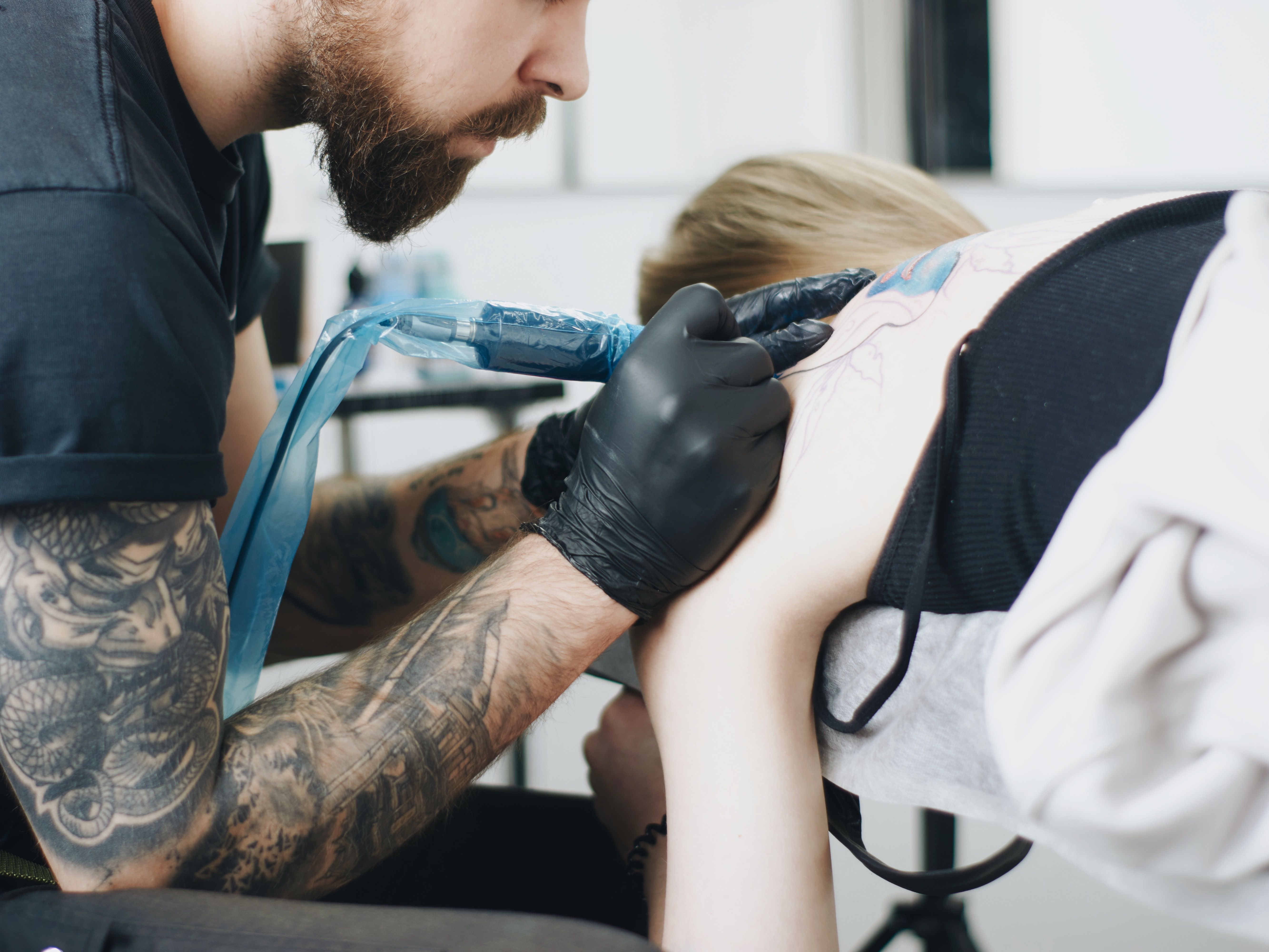 Tatuador concentrado tatuando o ombro de um cliente